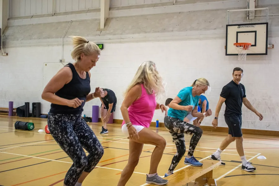 Class members doing step-ups on benches while Paul coaches them in the sports hall
